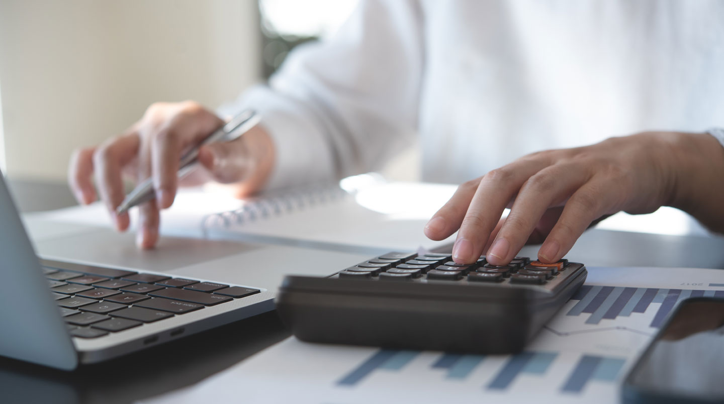 Vue de dessus d'un bureau avec relevé URSSAF, calculatrice et cahier de comptes lors du calcul des cotisations sociales provisionnelles